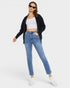Woman wearing a black jacket, white crop top, blue jeans, and sunglasses on a white background