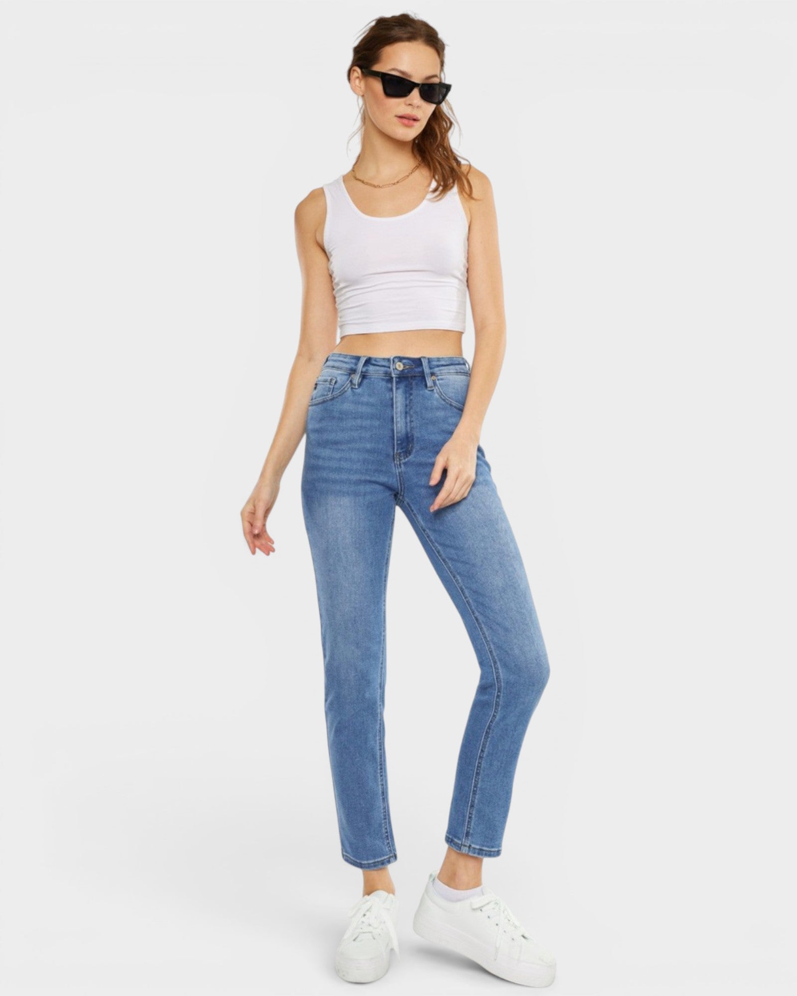 Woman wearing a white tank top and blue jeans on a white background