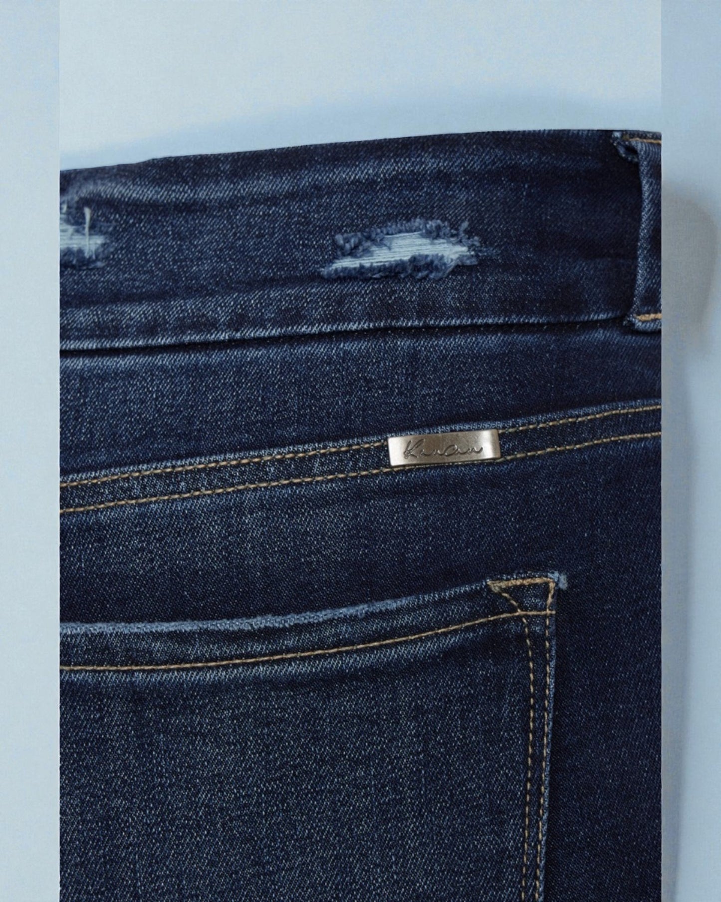 Close-up of dark blue jeans with a brand logo on a light gray background