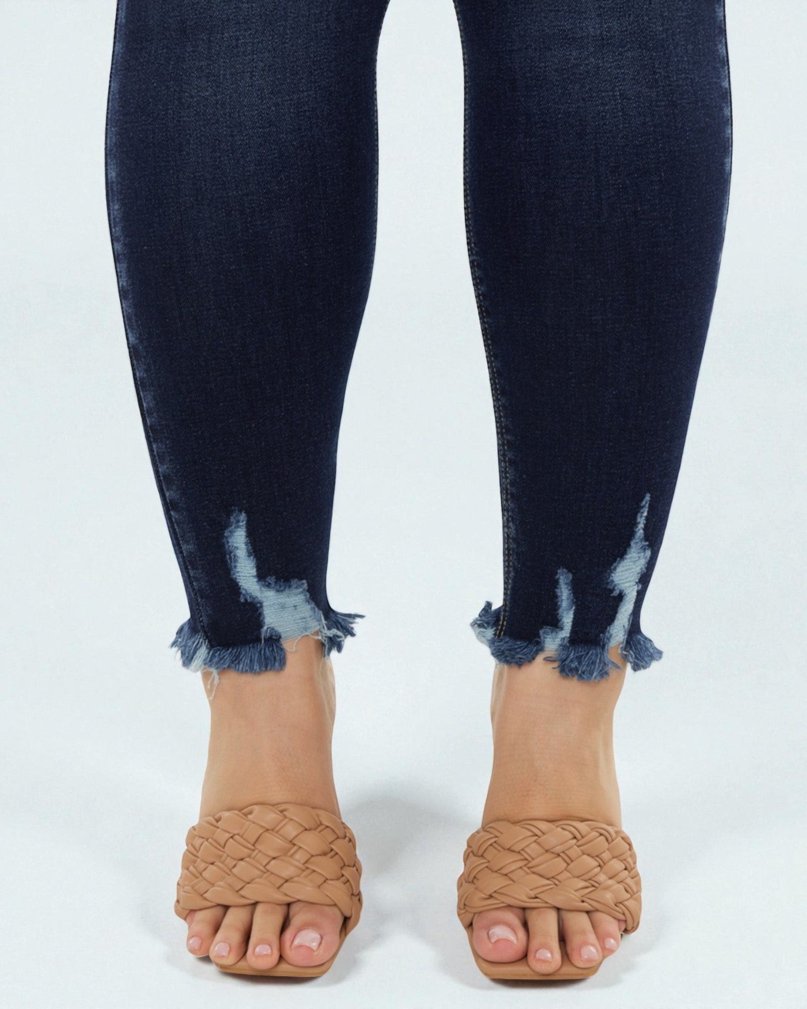 Person wearing dark blue distressed jeans with beige sandals on a white background