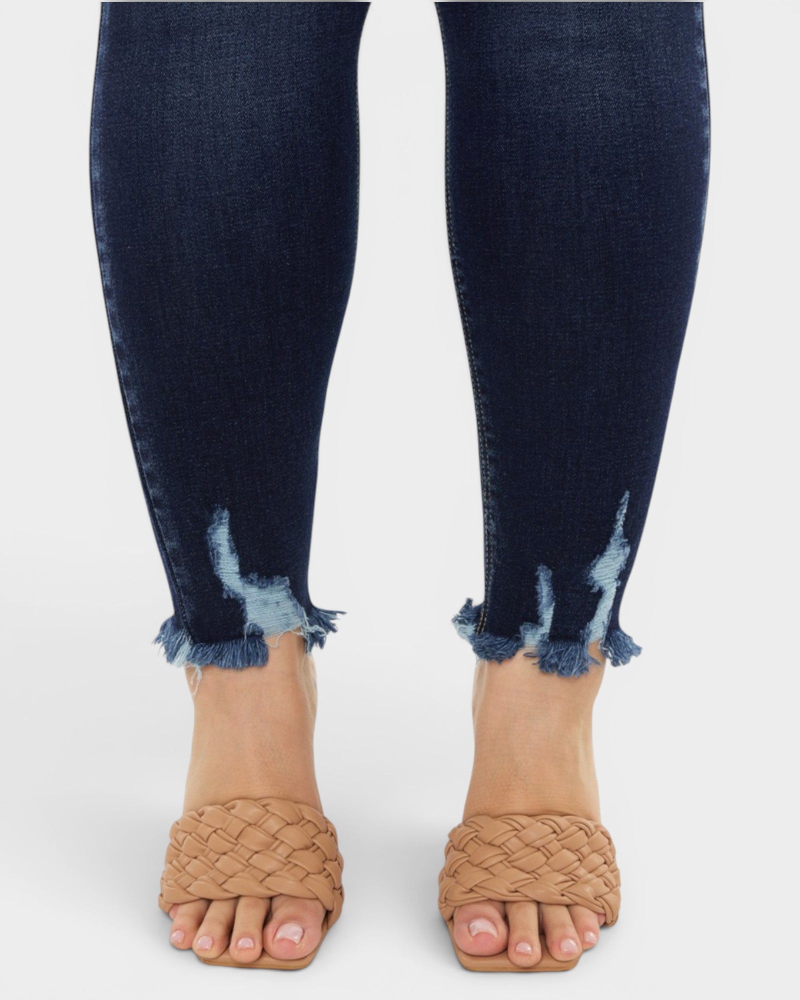Navy blue distressed jeans worn with tan woven sandals on a white background