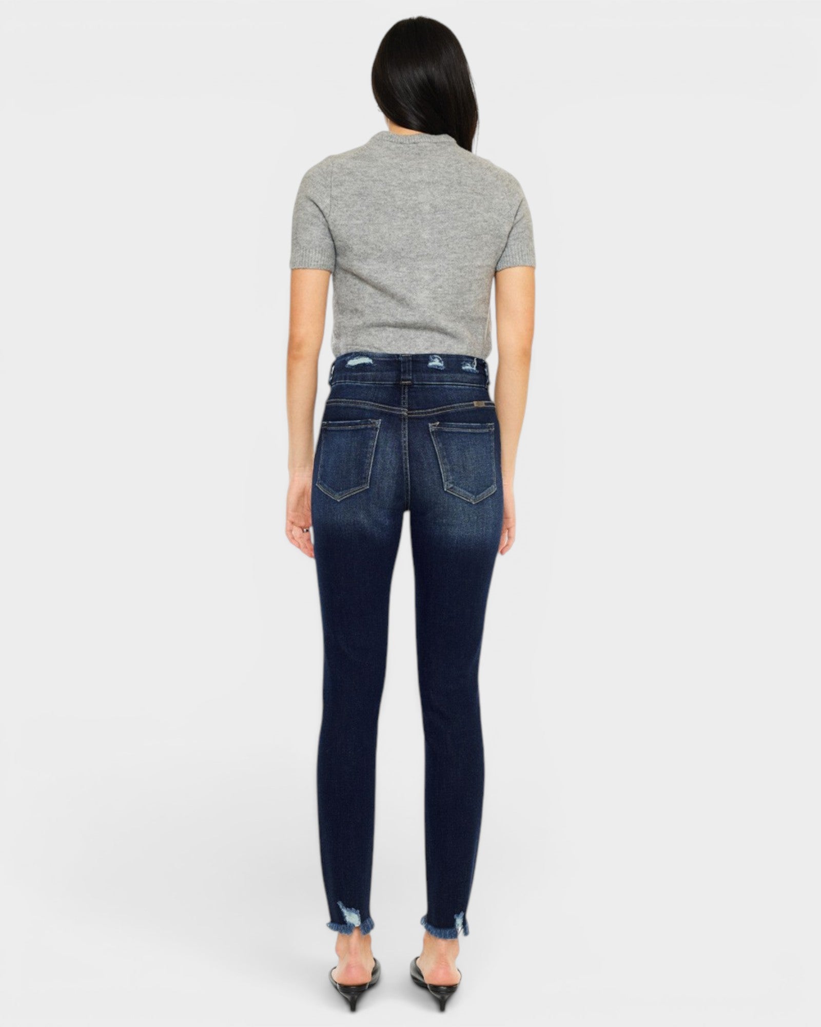 Person wearing dark blue jeans and a gray top on a white background
