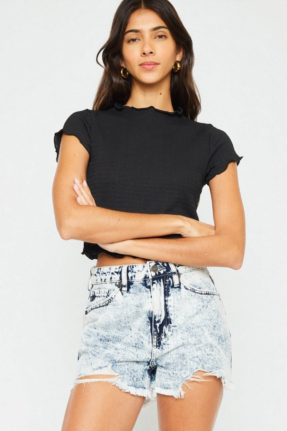 Woman wearing a black crop top and denim shorts on a plain background