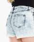 Close-up of the back of light-wash acid-wash denim shorts with a frayed hem, worn with a black ribbed top against a white background.