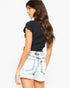 A woman shown from the back wearing a black short-sleeve top and light-wash distressed denim shorts against a plain white background.