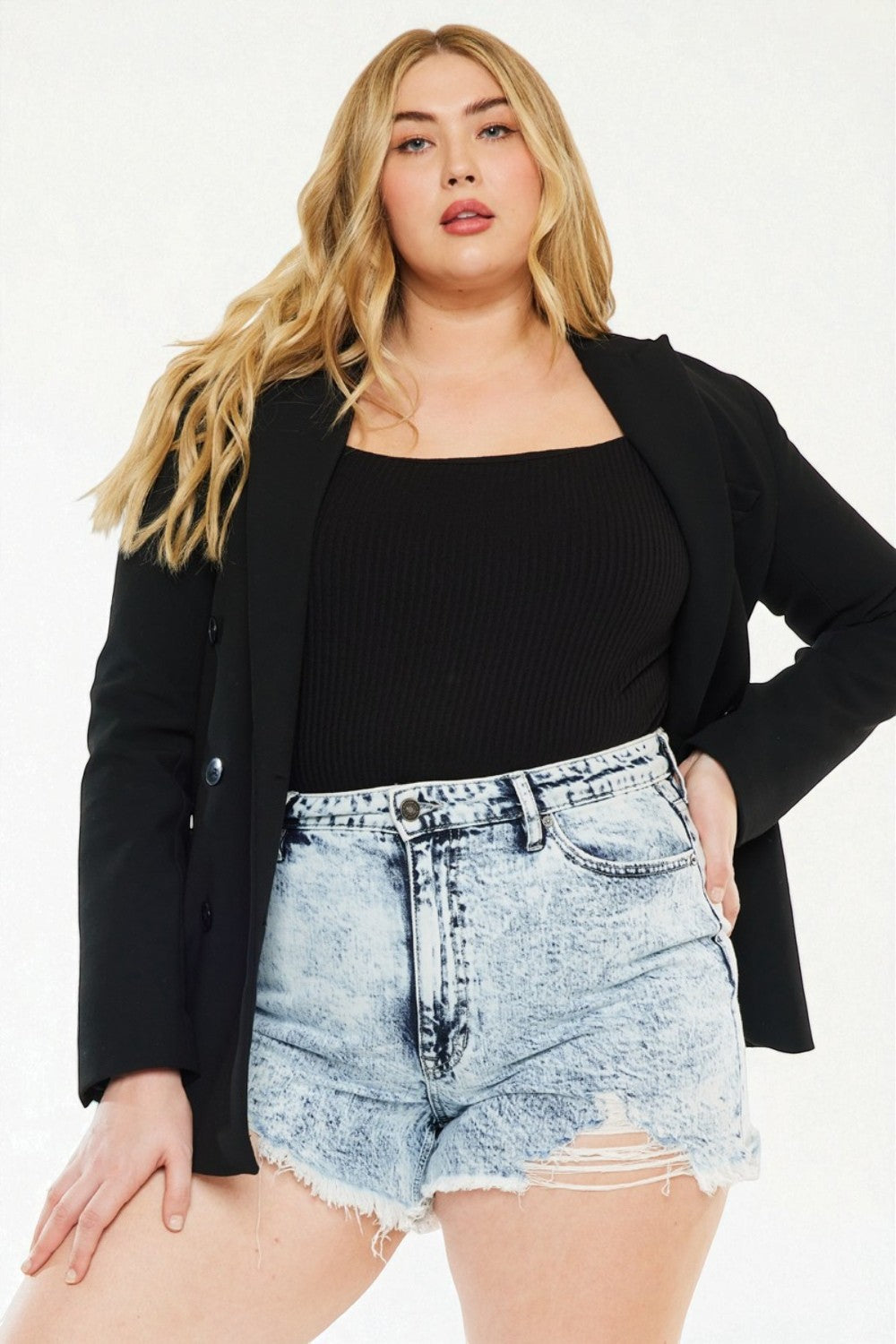 Woman wearing a black blazer, black top, and denim shorts on a white background