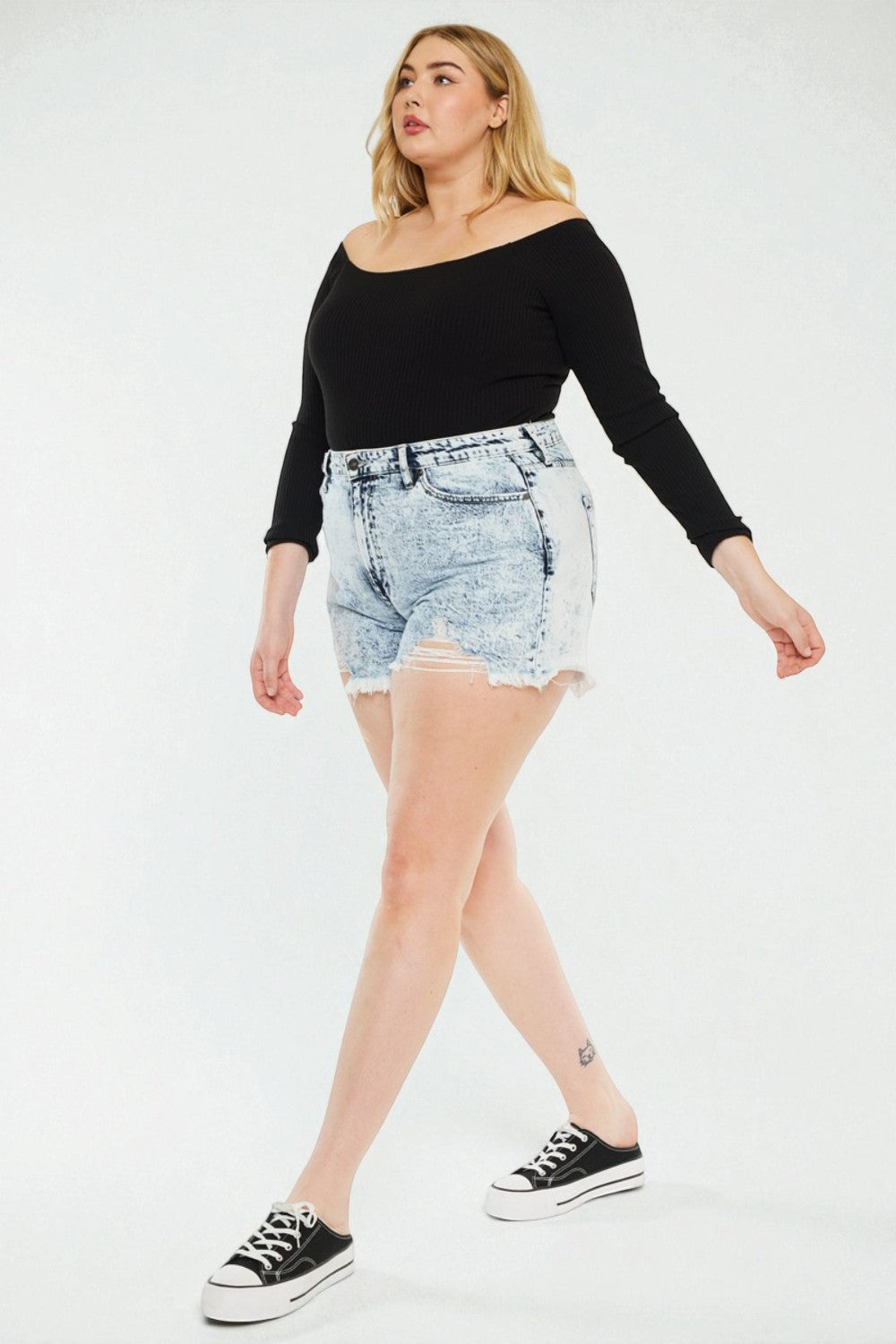 Woman wearing a black top and light blue denim shorts on a white background