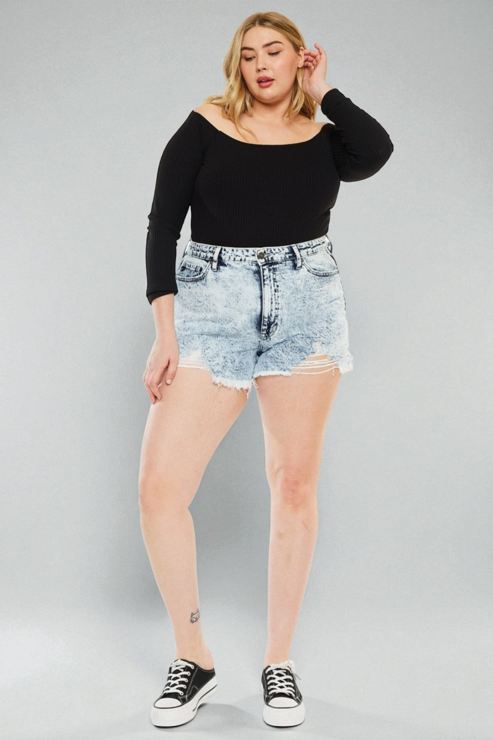Woman wearing a black top and denim shorts on a gray background