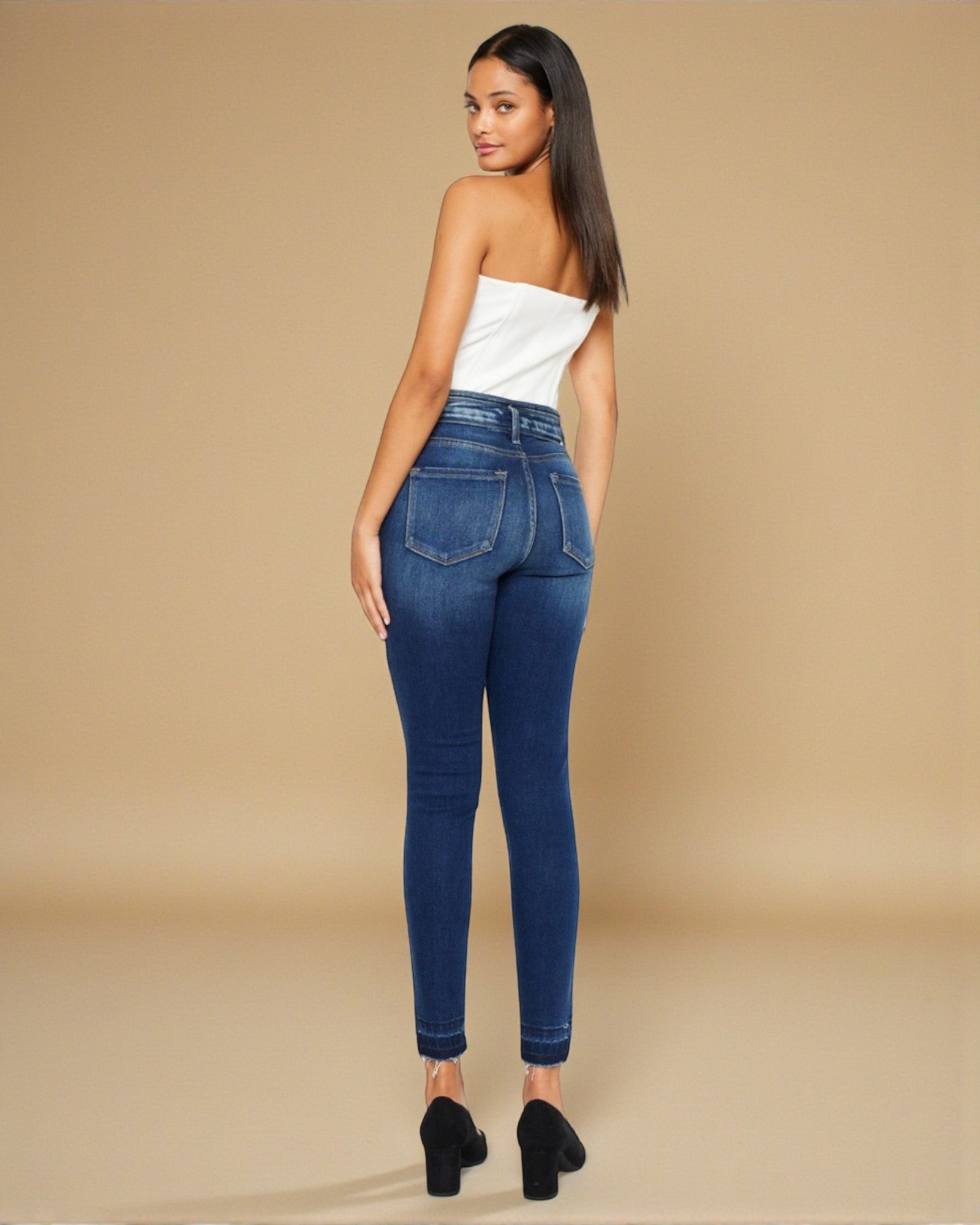 Woman wearing blue jeans and a white top on a beige background