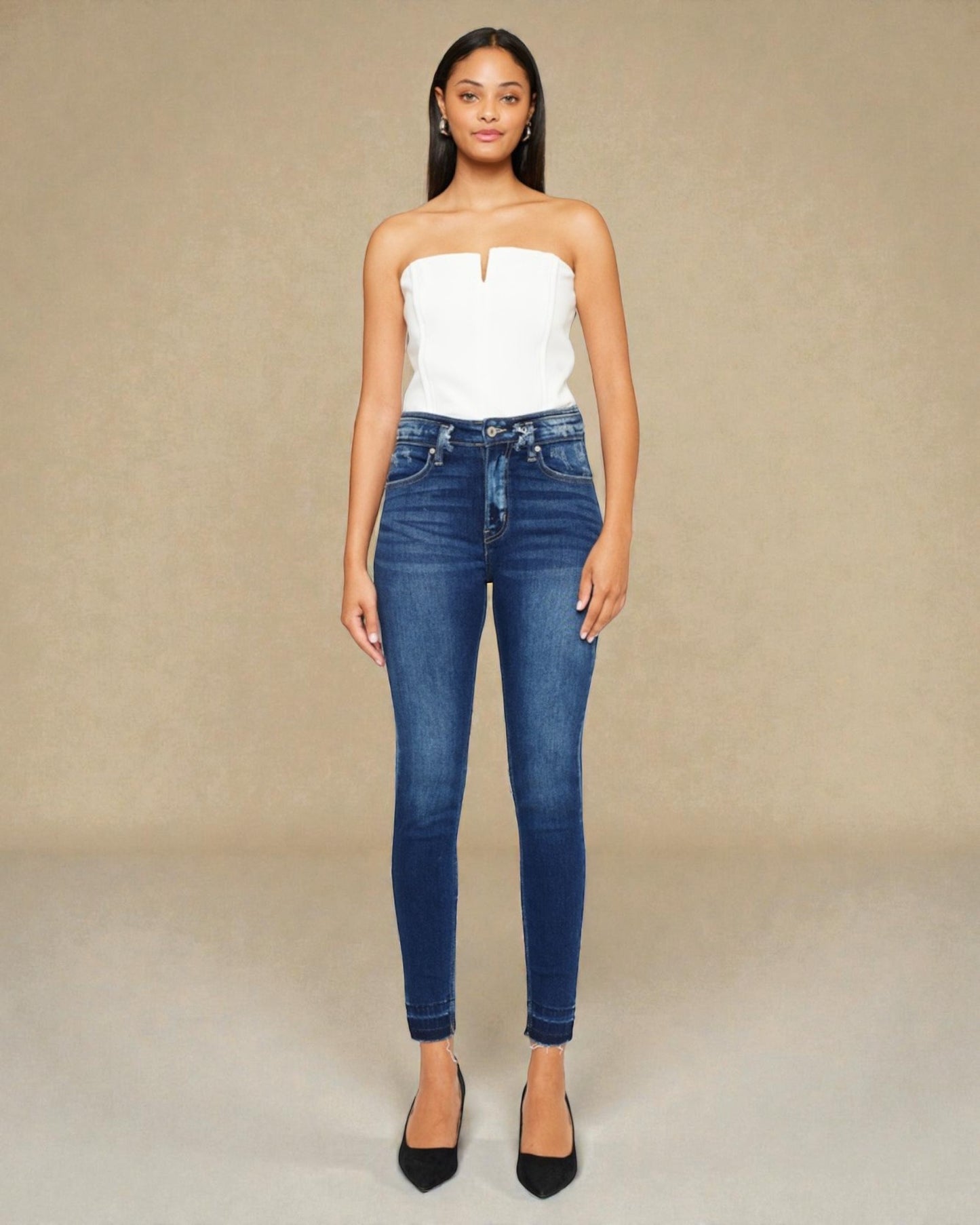 Woman wearing a white strapless top and blue jeans against a beige background