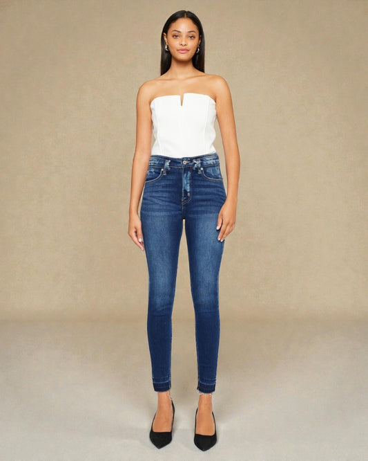 Woman wearing a white strapless top and blue jeans against a beige background