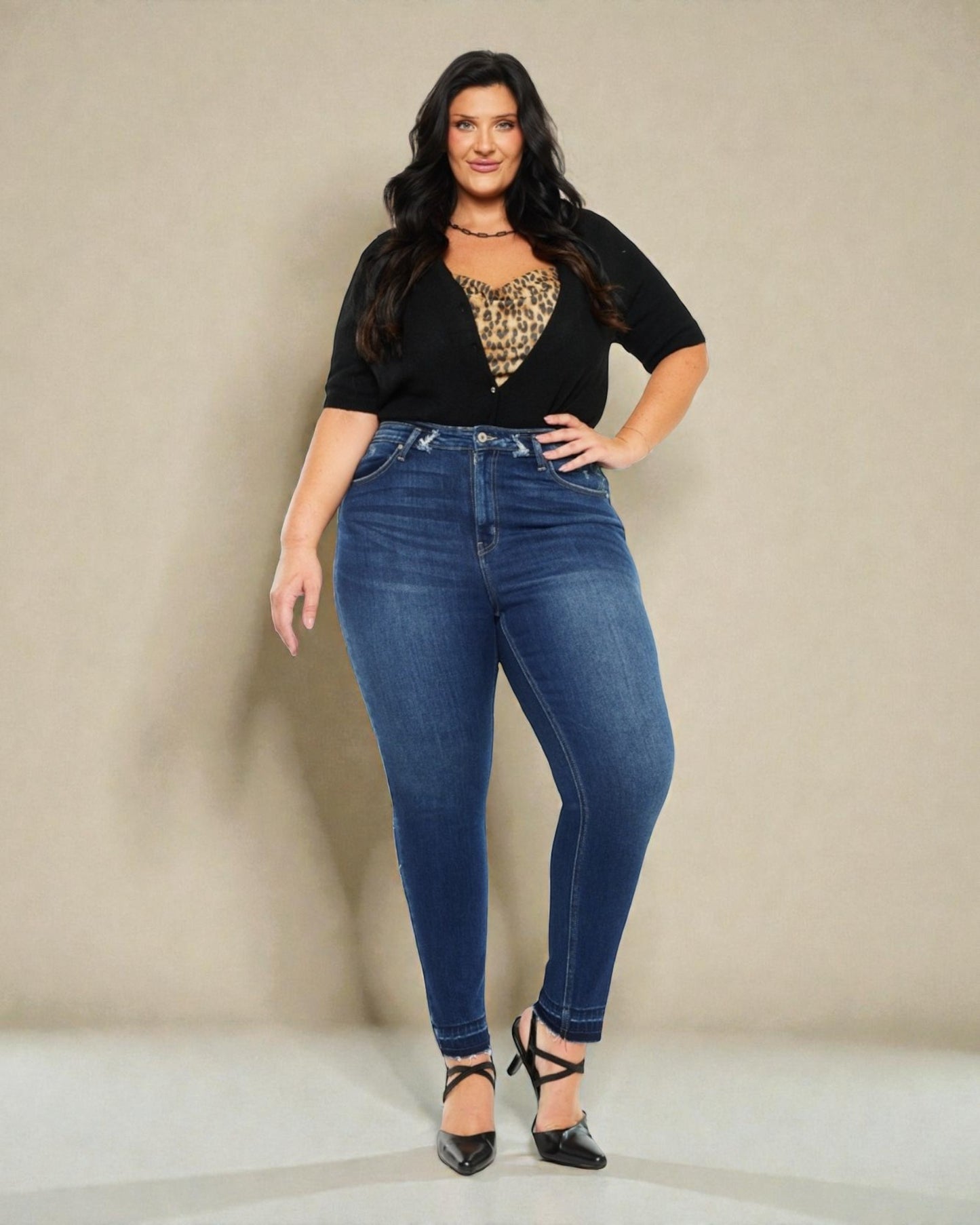 Woman wearing blue jeans and a black top with a patterned design against a beige background