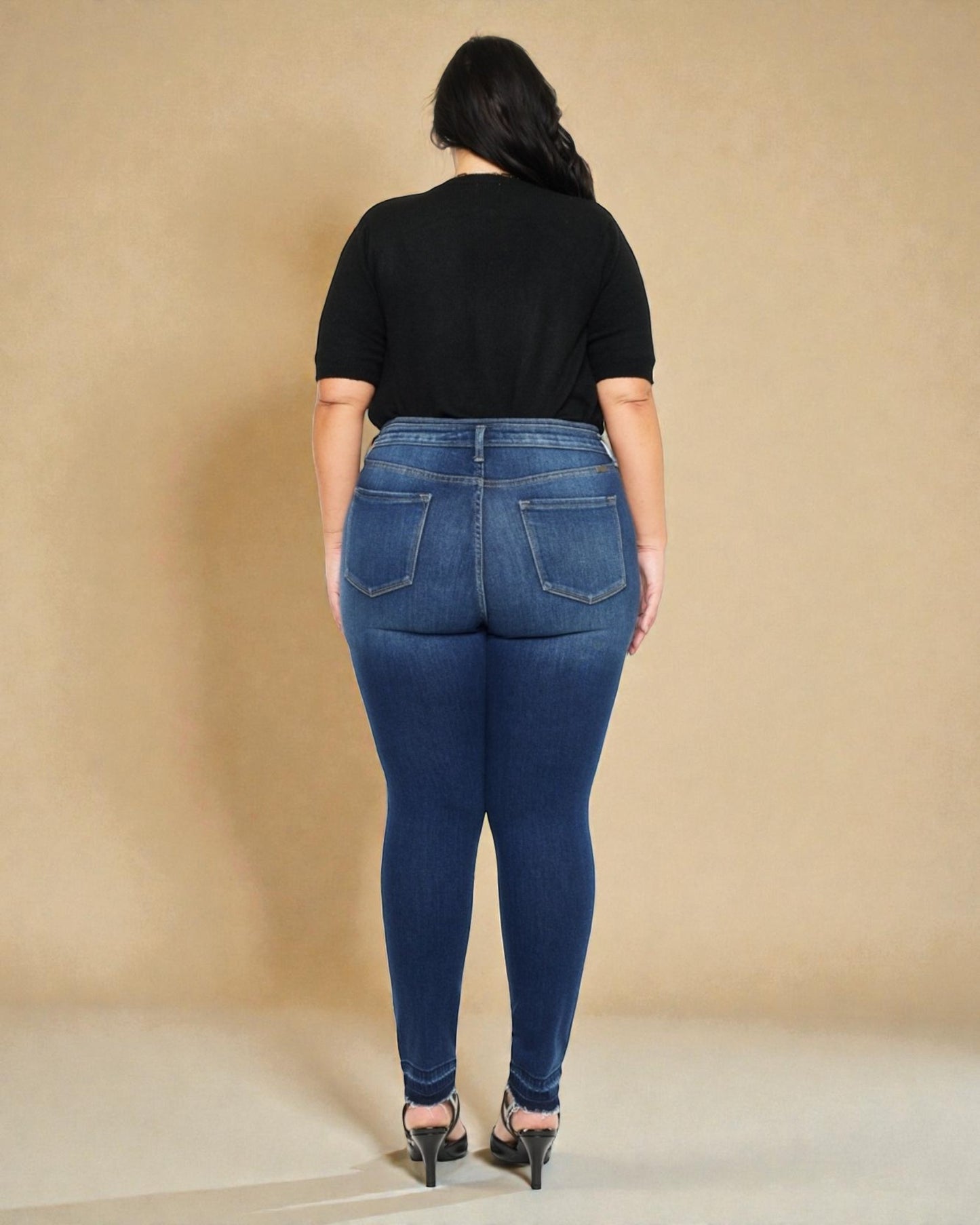 Person wearing blue jeans and a black top against a beige background