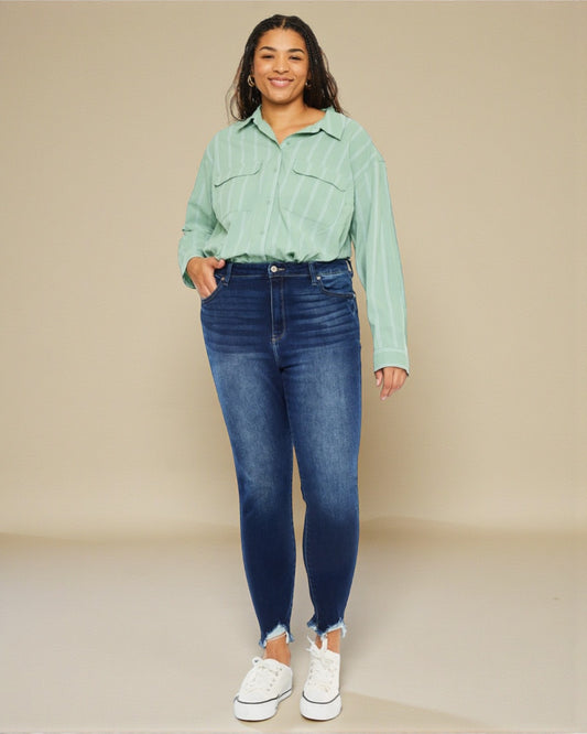 Woman wearing a light green shirt and blue jeans against a beige background
