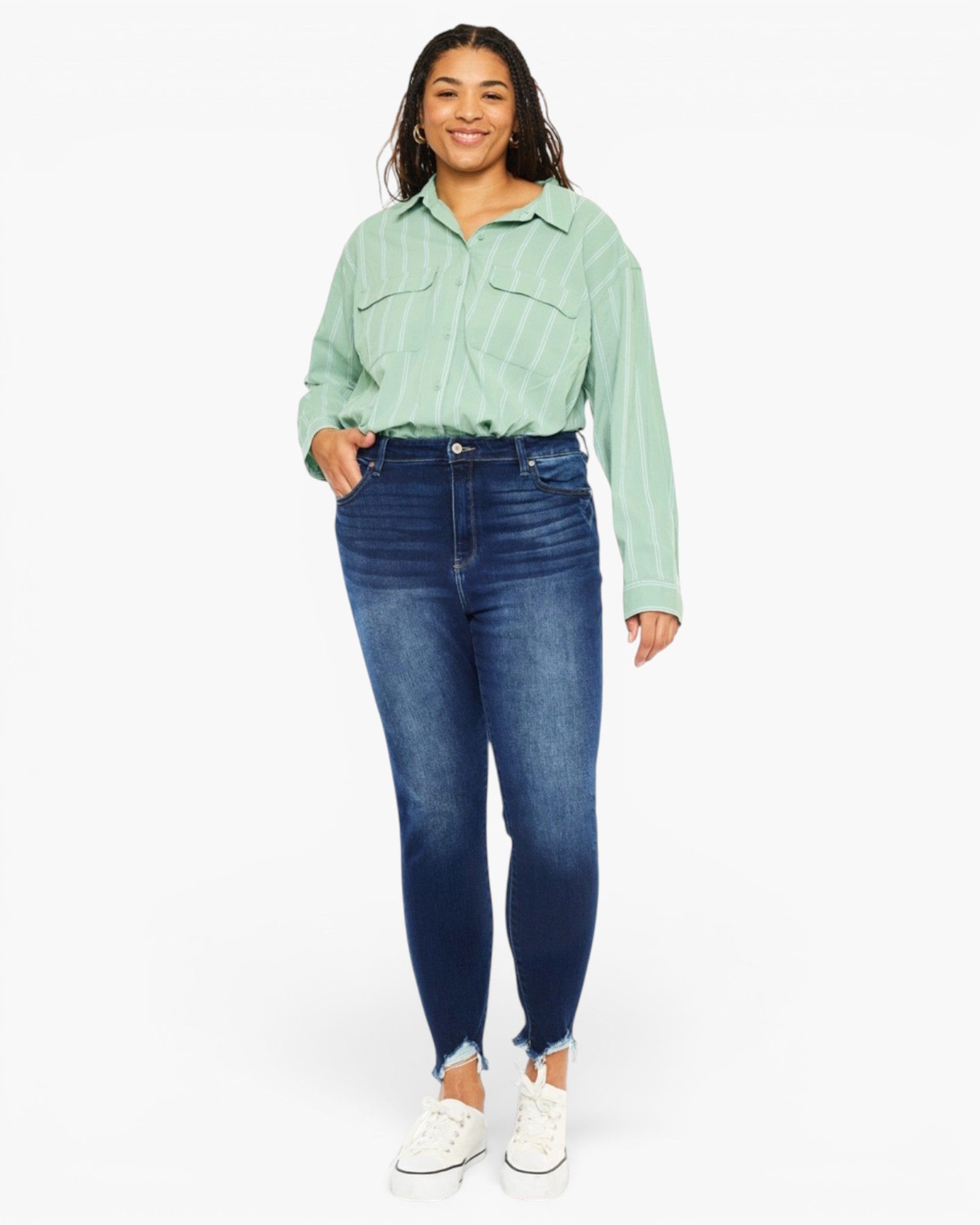 A woman modeling a light green striped button-up shirt and dark blue skinny jeans with white sneakers, photographed against a plain light gray studio background.
