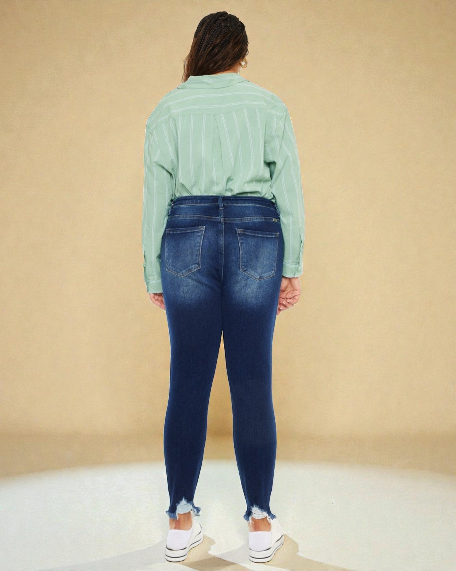Person wearing a green shirt and blue jeans against a beige background