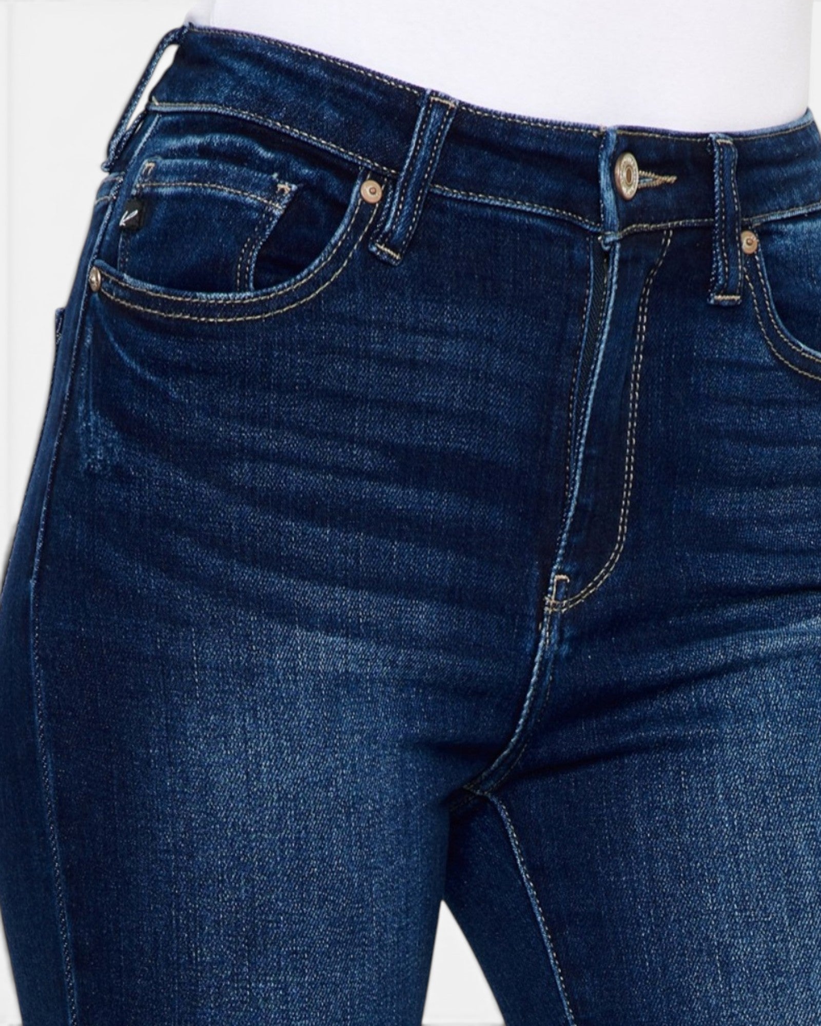 Close-up of dark blue denim jeans with visible front pockets, belt loops, button, and contrast stitching on a white background.