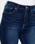 Close-up of dark blue denim jeans with visible front pockets, belt loops, button, and contrast stitching on a white background.