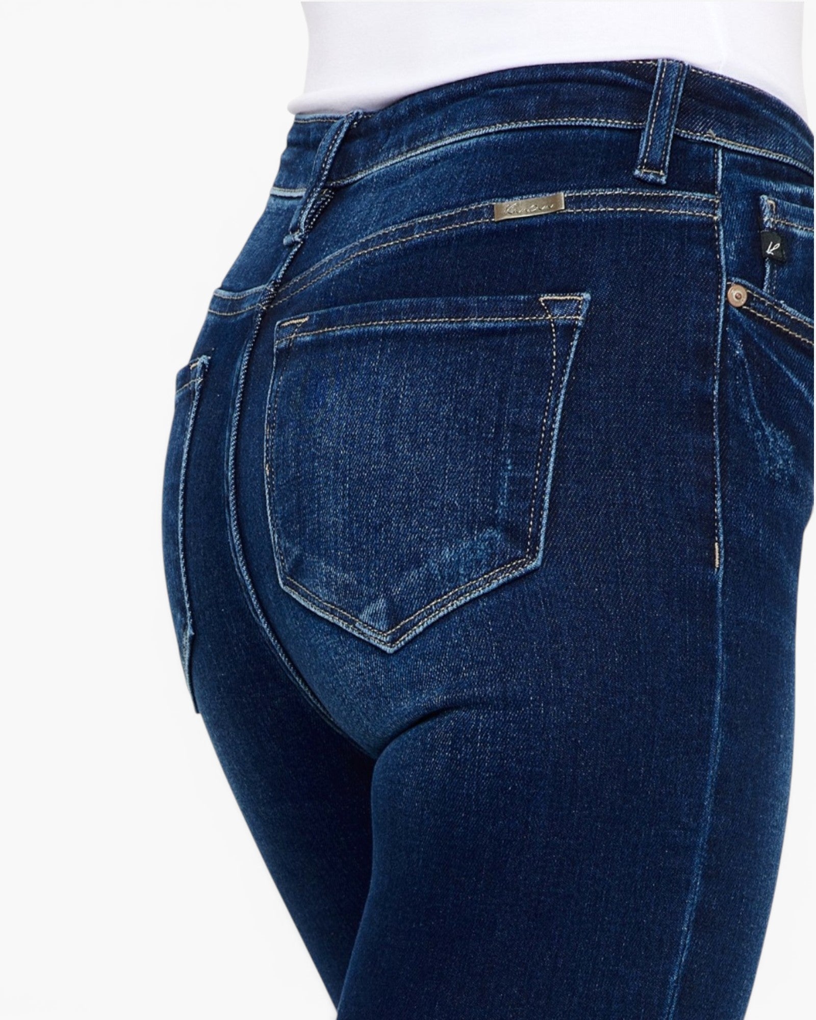 Close-up back view of dark blue denim jeans on a model, showing the back pockets, belt loops, and waistband against a plain white background.