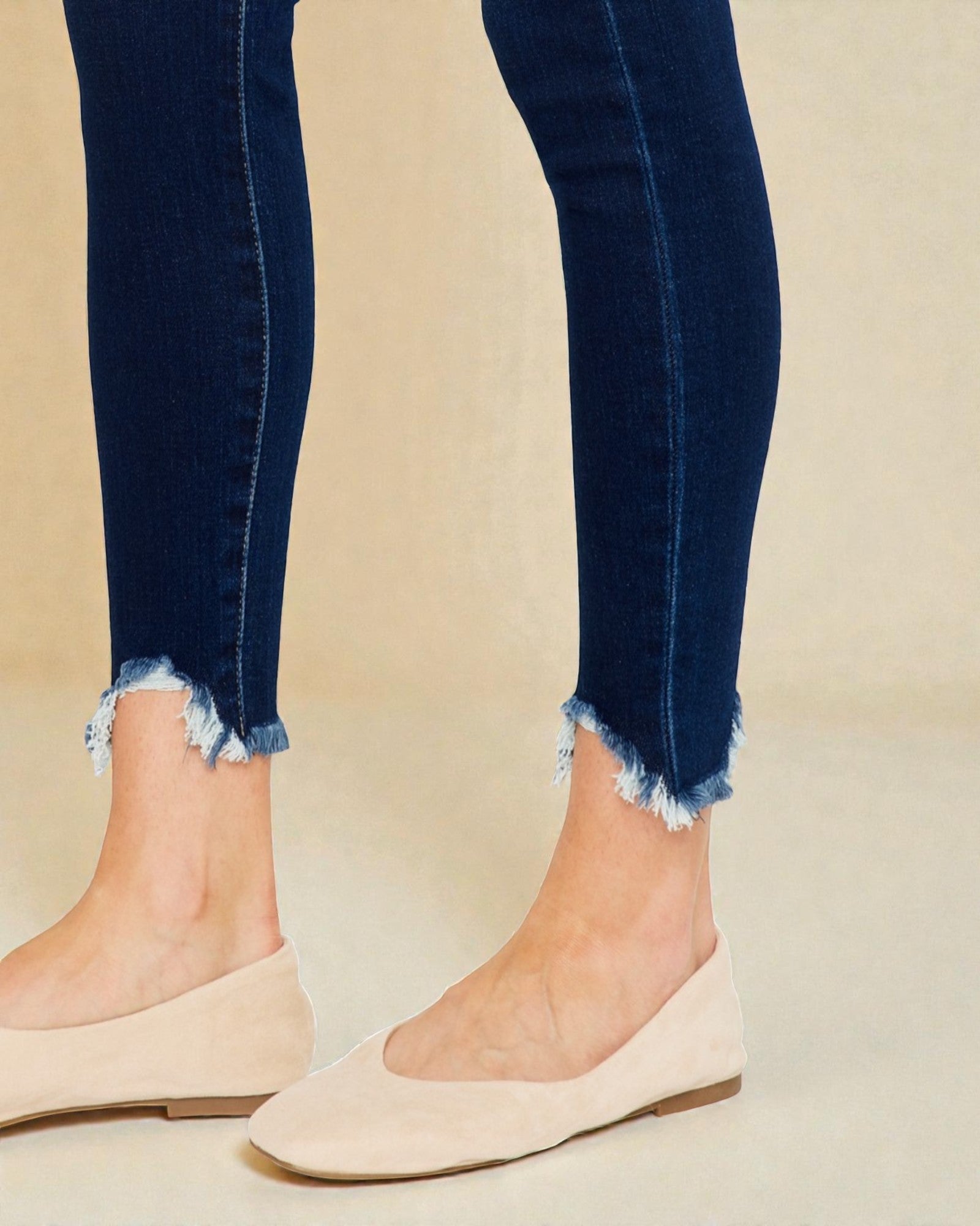 Person wearing blue jeans with frayed cuffs and beige flats on a beige background