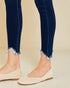 Person wearing blue jeans with frayed cuffs and beige flats on a beige background