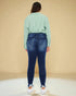 Person wearing a green shirt and blue jeans against a beige background