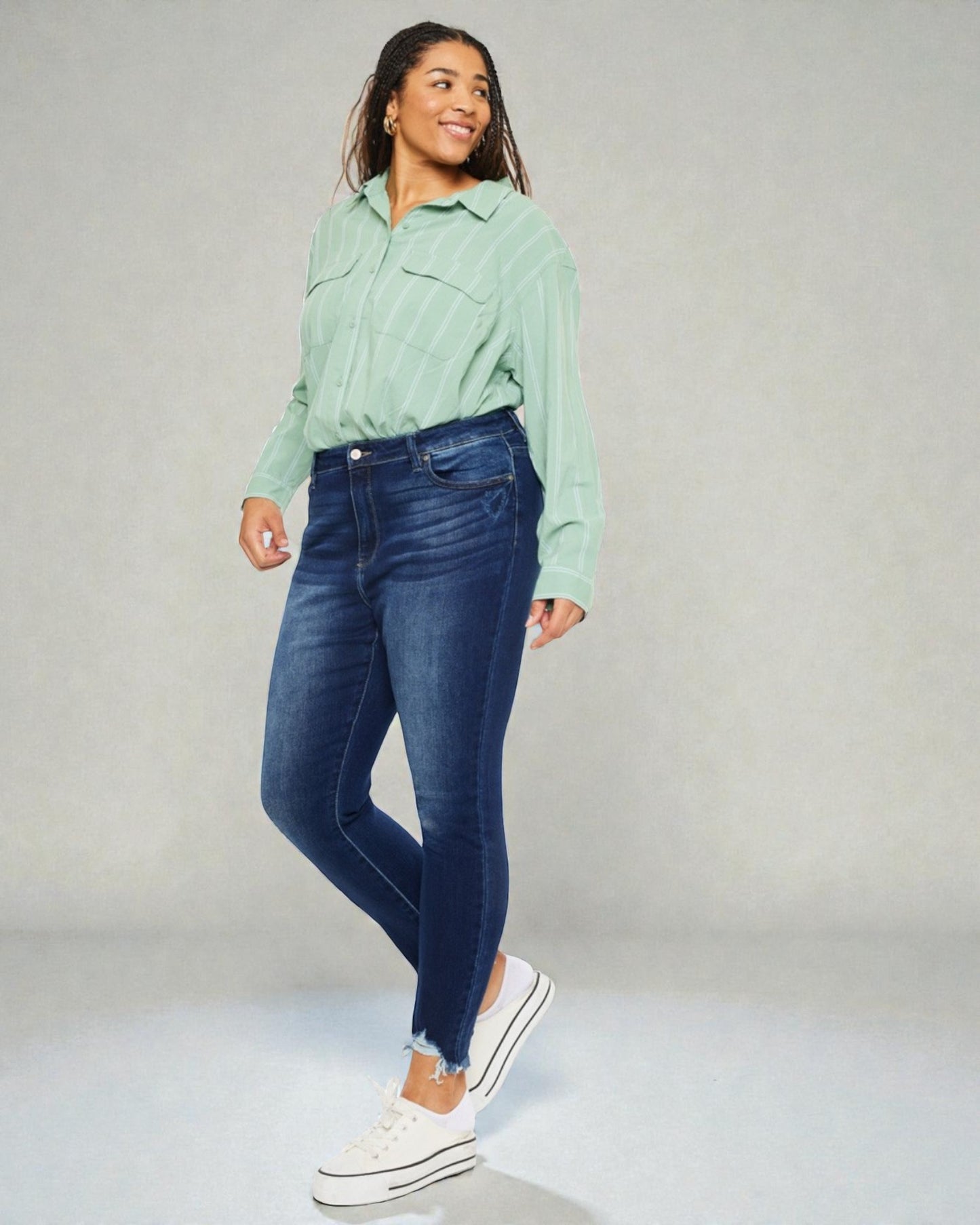Woman wearing a green shirt and blue jeans against a gray background