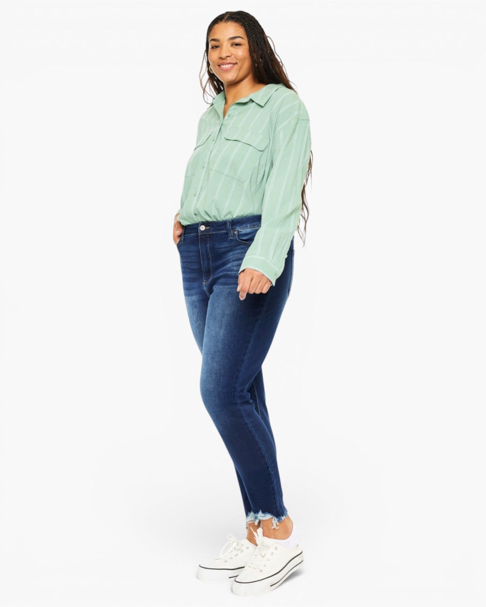 A woman modeling a mint green striped long-sleeve button-up shirt and dark blue skinny jeans with white sneakers, photographed against a plain white studio background.