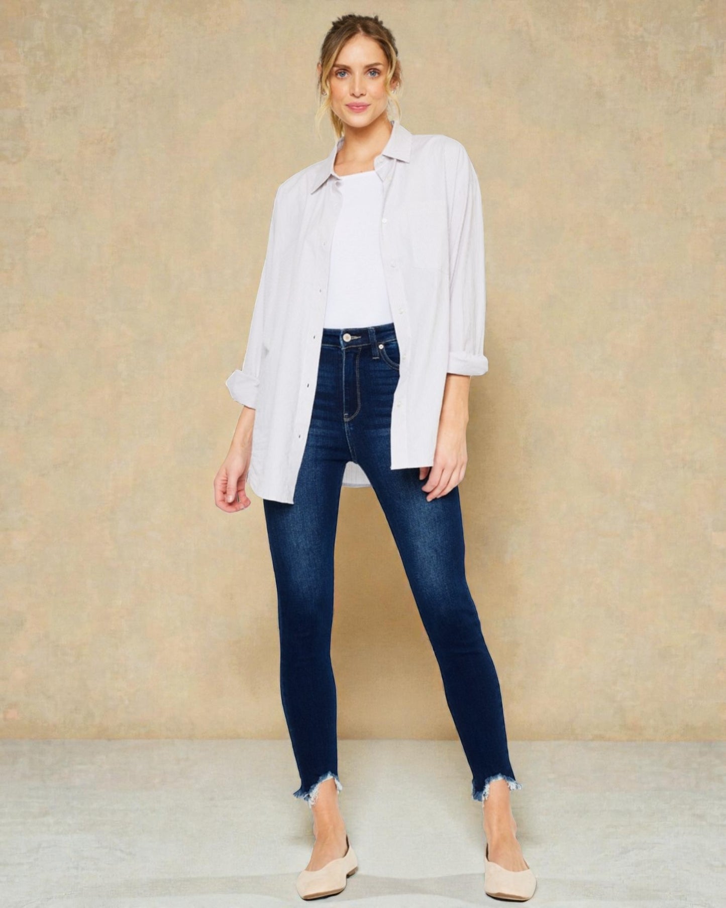 Woman wearing a white shirt and blue jeans against a beige background