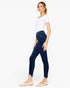 A woman modeling dark wash skinny jeans with a frayed hem, paired with a white top and beige flats, shown from a side profile against a light gray background.