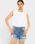 Woman wearing a white sleeveless top and denim shorts on a light gray background
