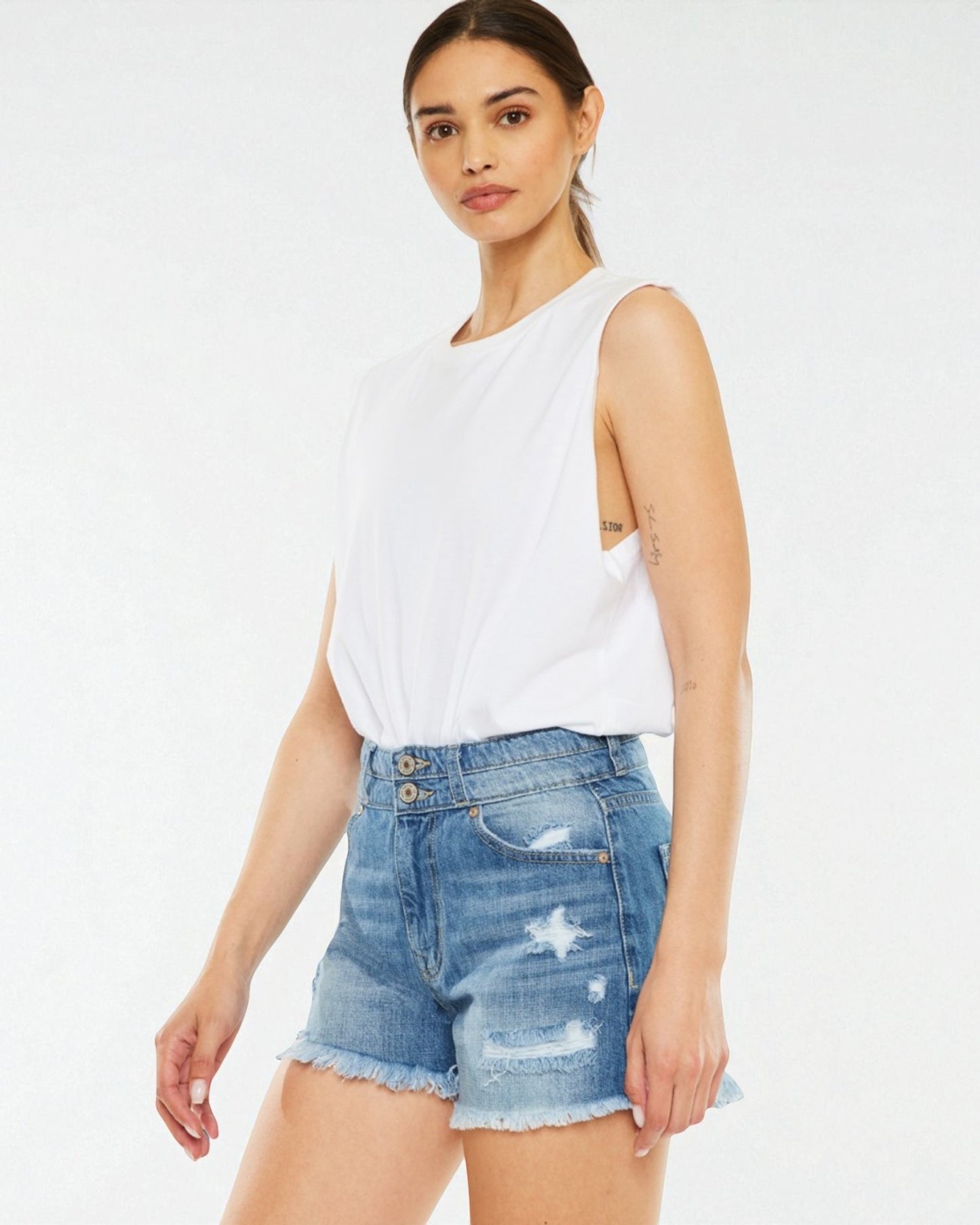 Woman wearing a white sleeveless top and denim shorts on a white background