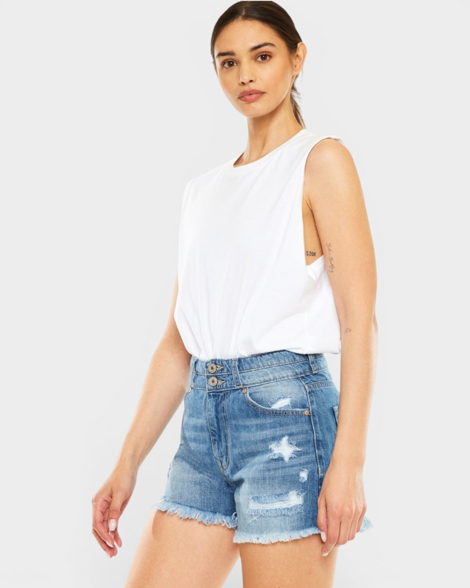 Woman wearing a white sleeveless top and denim shorts on a plain background