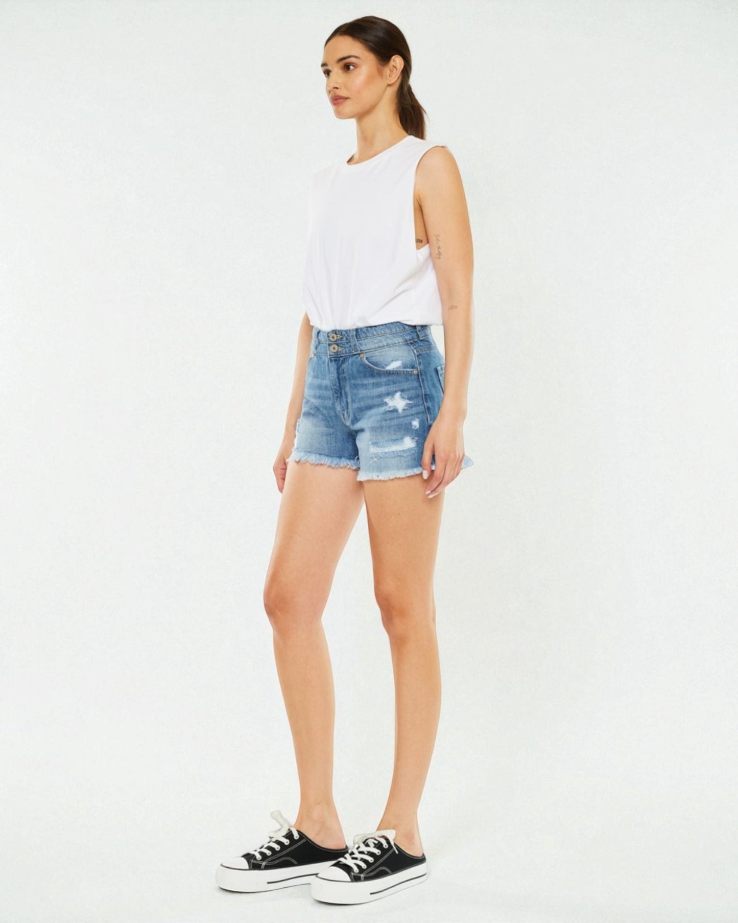 Woman wearing a white sleeveless top and blue denim shorts on a white background