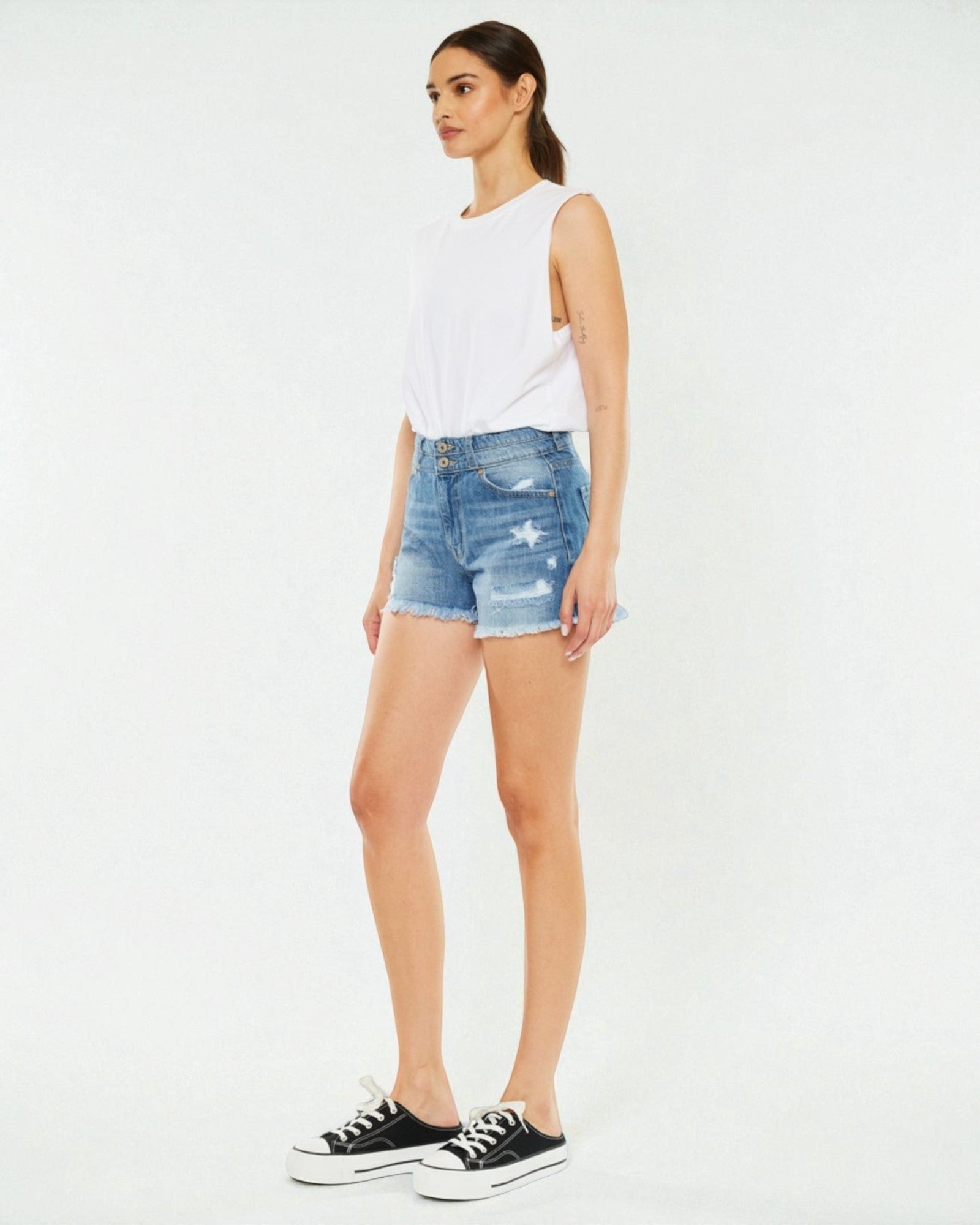 Woman wearing a white sleeveless top and blue denim shorts on a white background