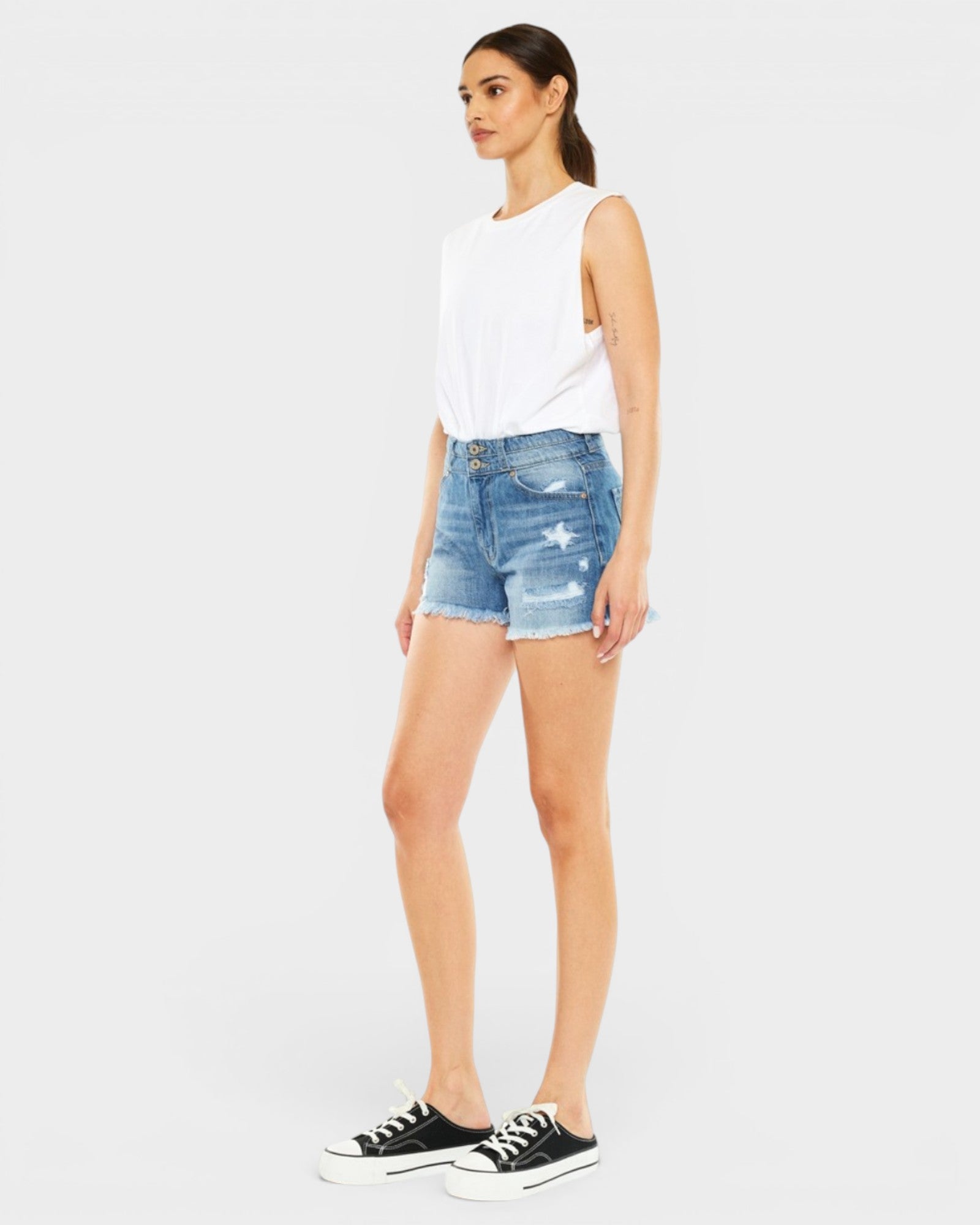 Woman wearing a white sleeveless top and blue denim shorts on a white background