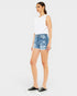 Woman wearing a white sleeveless top and blue denim shorts on a white background