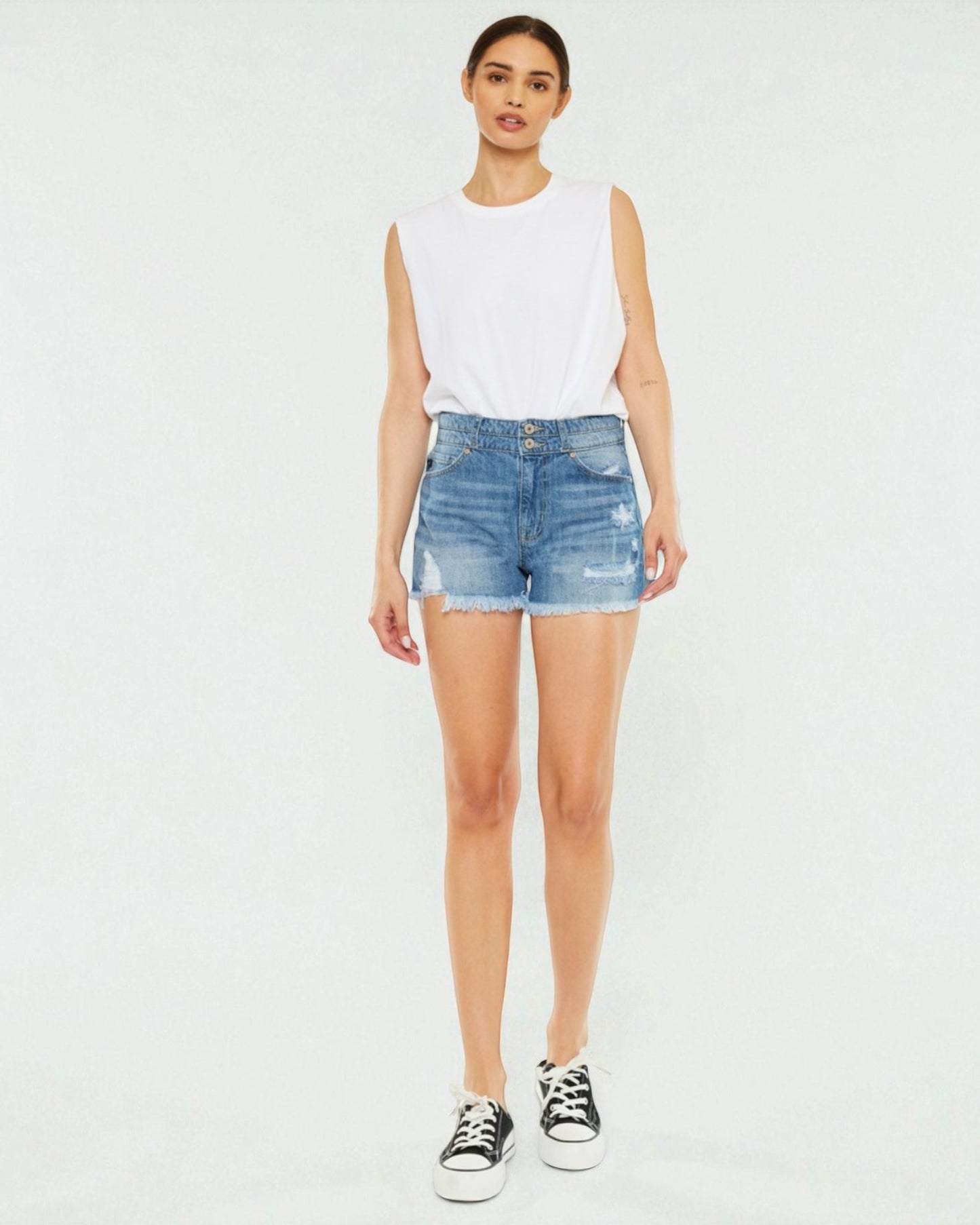 Woman wearing a white sleeveless top and denim shorts on a white background