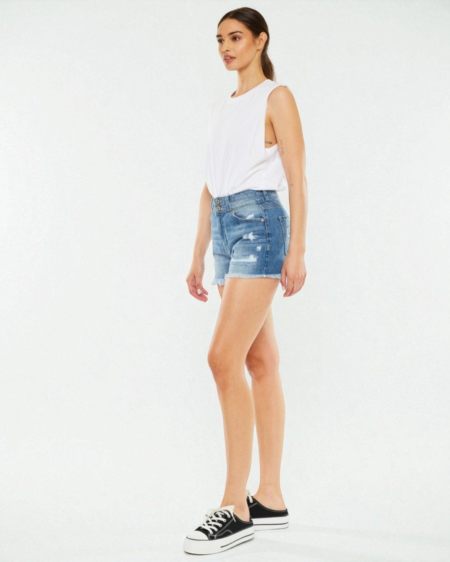 Woman wearing a white sleeveless top and blue denim shorts on a white background