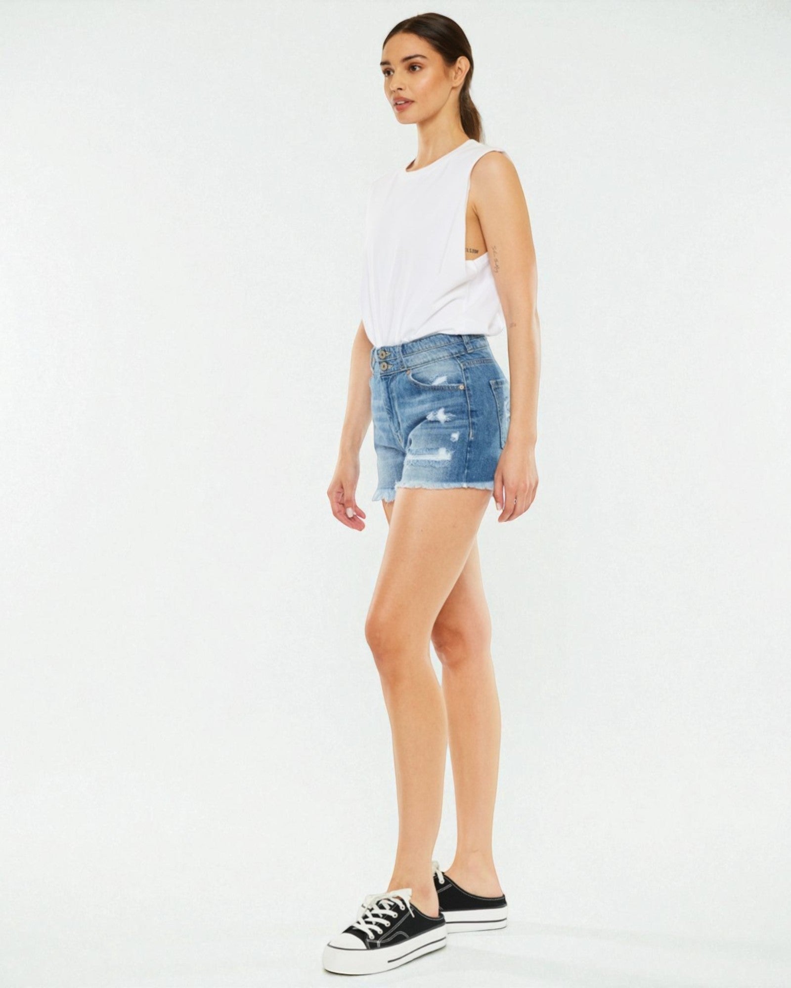 Woman wearing a white sleeveless top and blue denim shorts on a white background
