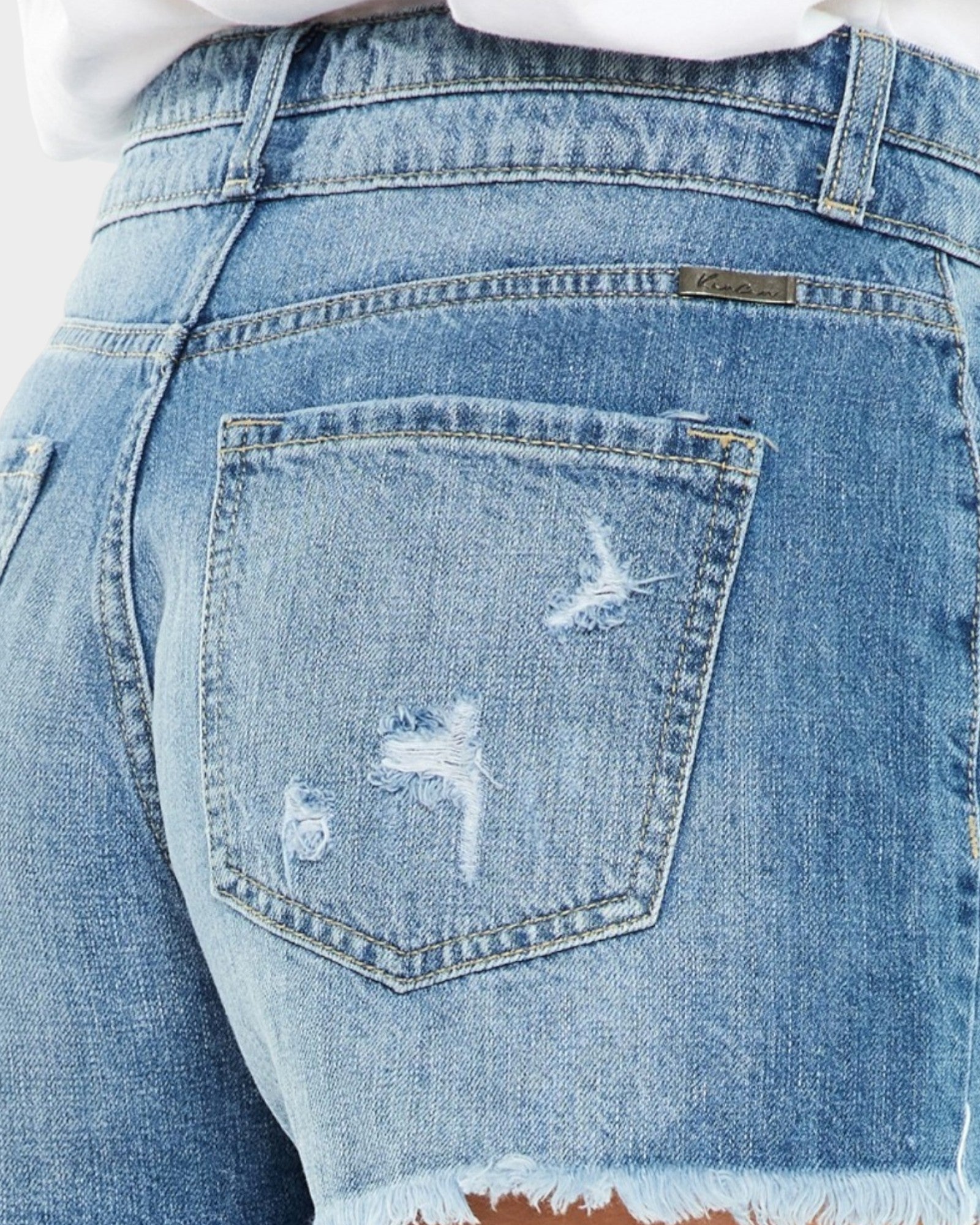 Close-up of a distressed blue denim pocket with a brand logo.