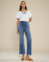 Woman wearing a white embroidered top and blue jeans on a beige background
