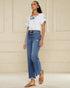 Woman wearing a white embroidered top and blue jeans against a beige wall.