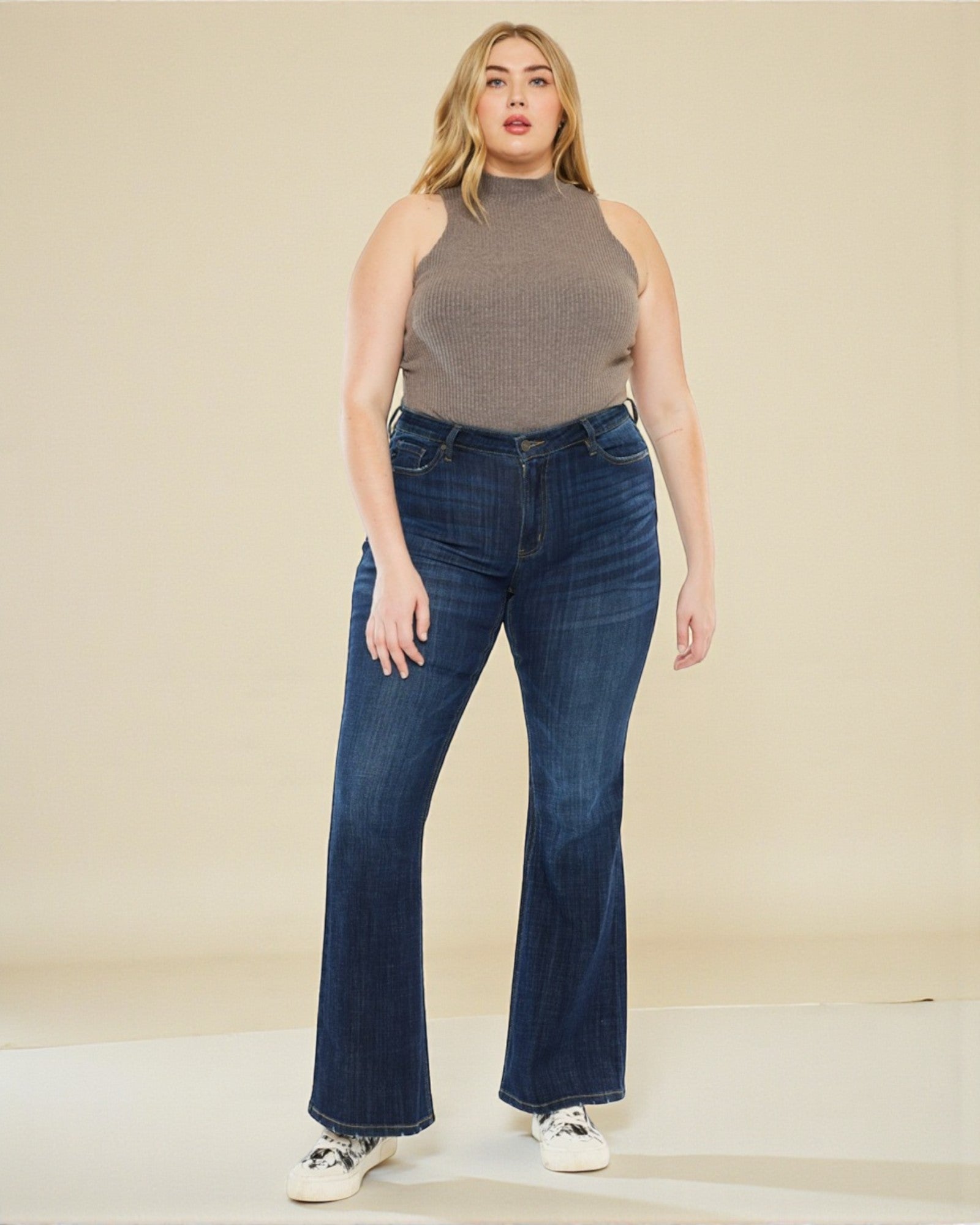 Woman wearing a sleeveless brown top and blue jeans against a beige background