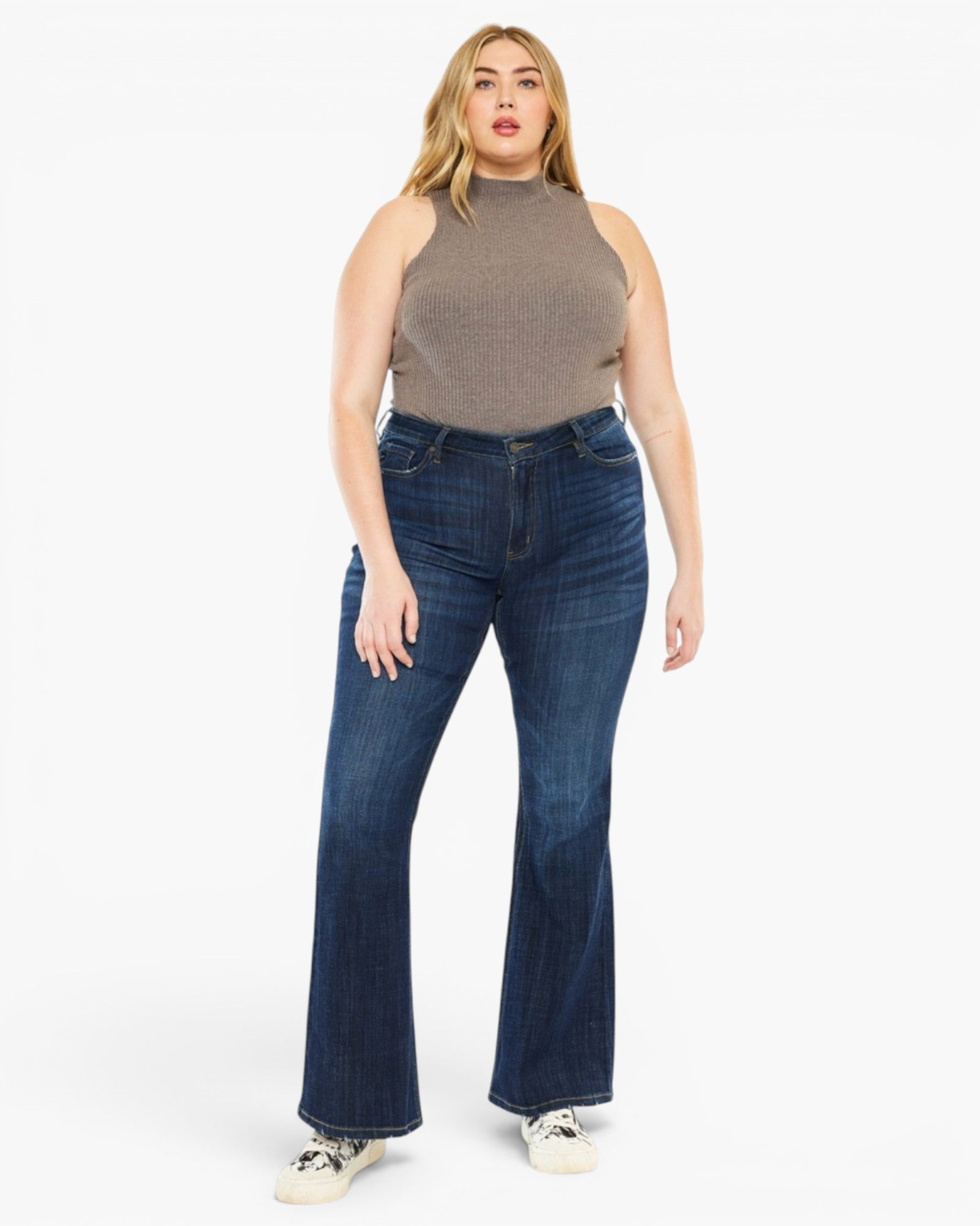 A woman modeling a pair of dark blue high-waisted flare jeans with a ribbed knit sleeveless top, standing against a plain white studio background.