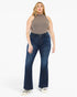 A woman modeling a pair of dark blue high-waisted flare jeans with a ribbed knit sleeveless top, standing against a plain white studio background.