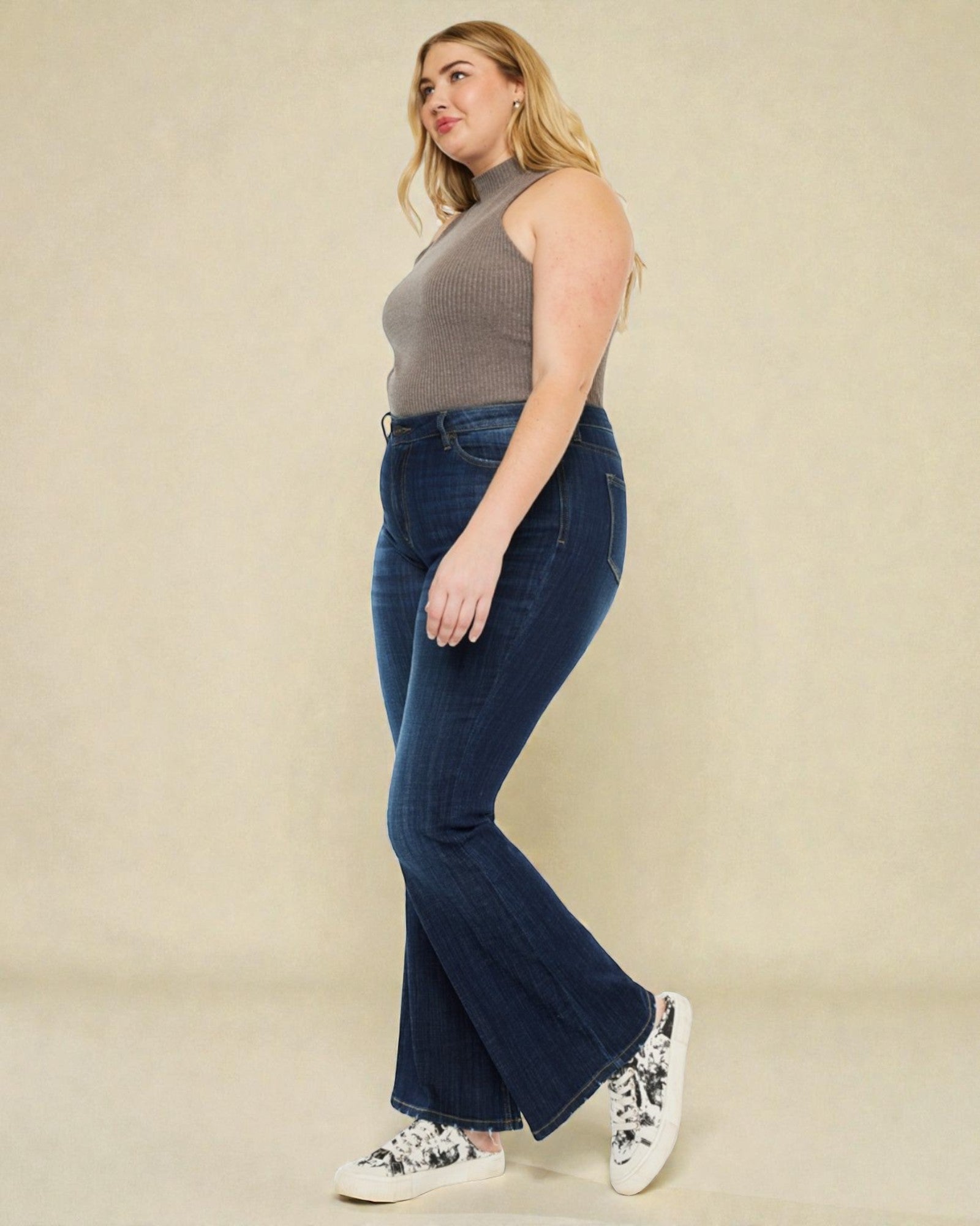 Woman wearing blue jeans and a gray top against a beige background