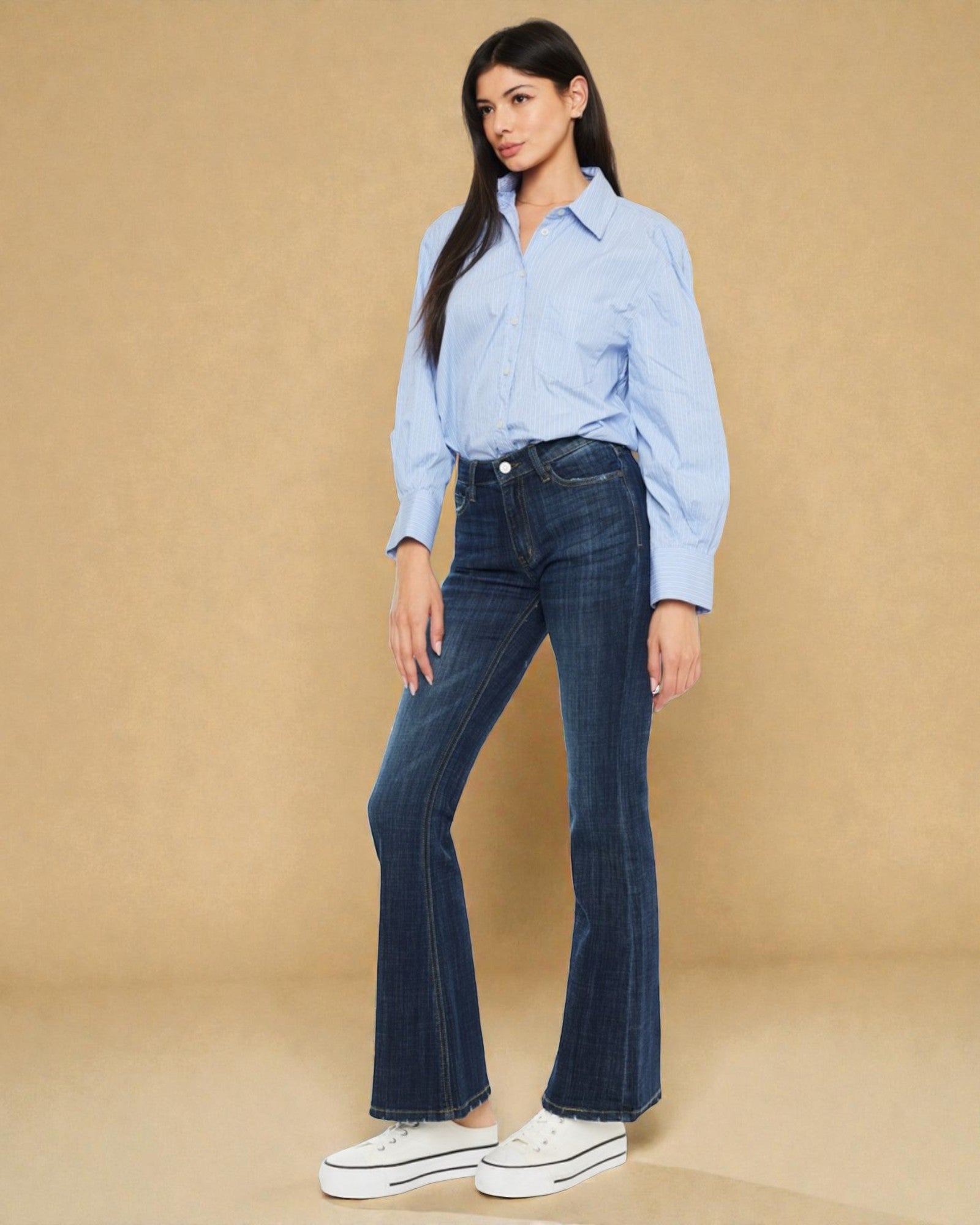 Woman wearing a light blue shirt and dark blue jeans against a beige background