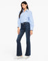 A woman modeling a light blue button-up shirt and dark blue flare jeans with white platform sneakers, photographed against a plain white studio background.