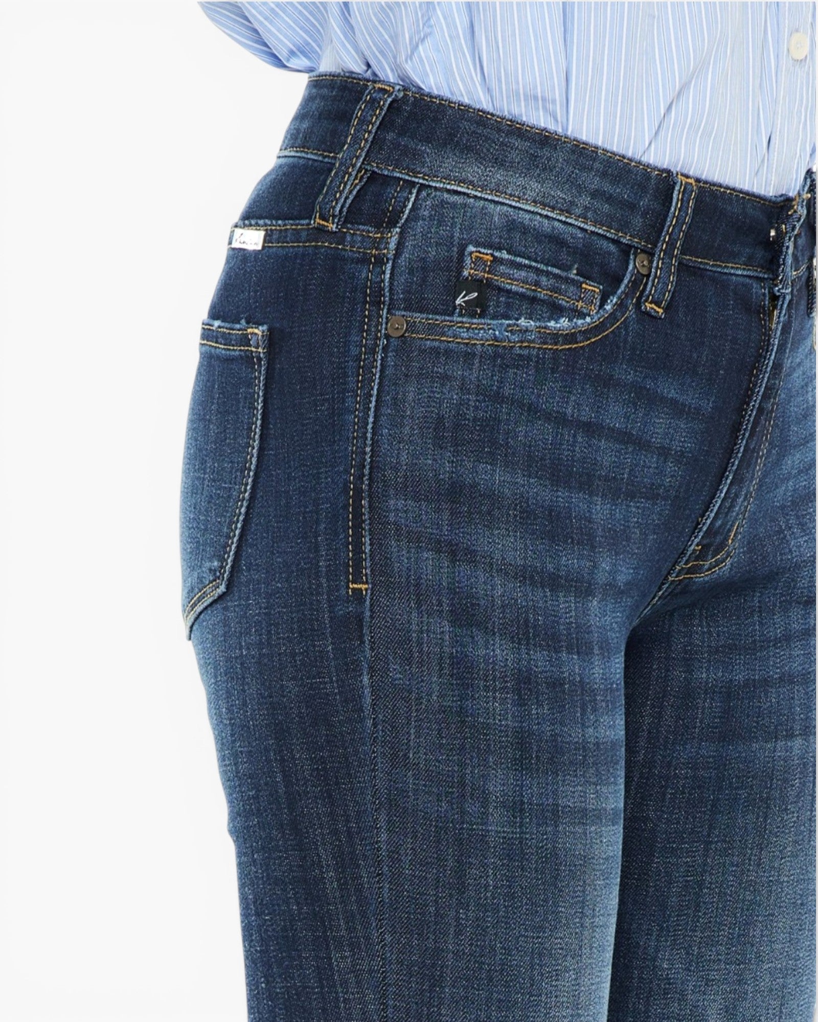 Close-up of a person wearing dark blue denim jeans with a light blue and white striped shirt visible at the waist, against a plain white background.